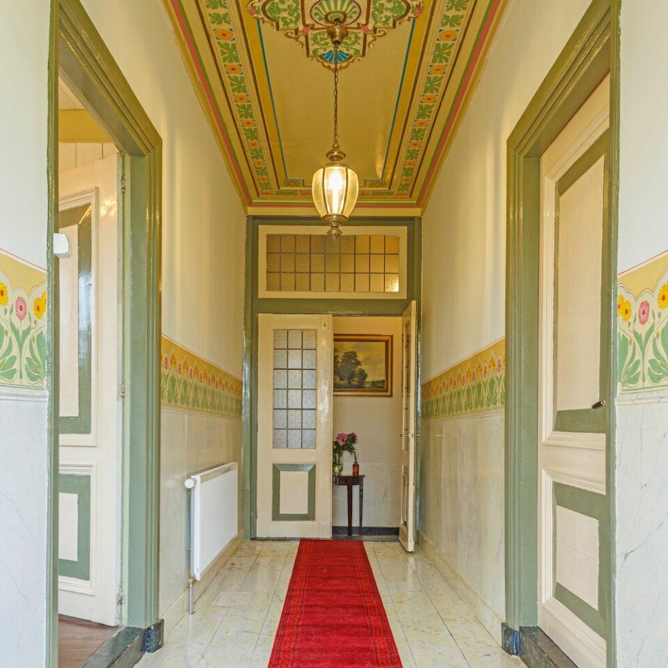 Statige en kleurrijke entreehal met gemarmerd geschilderde vloer en lambrisering met aan weerzijden de ‘pronkkamers’.