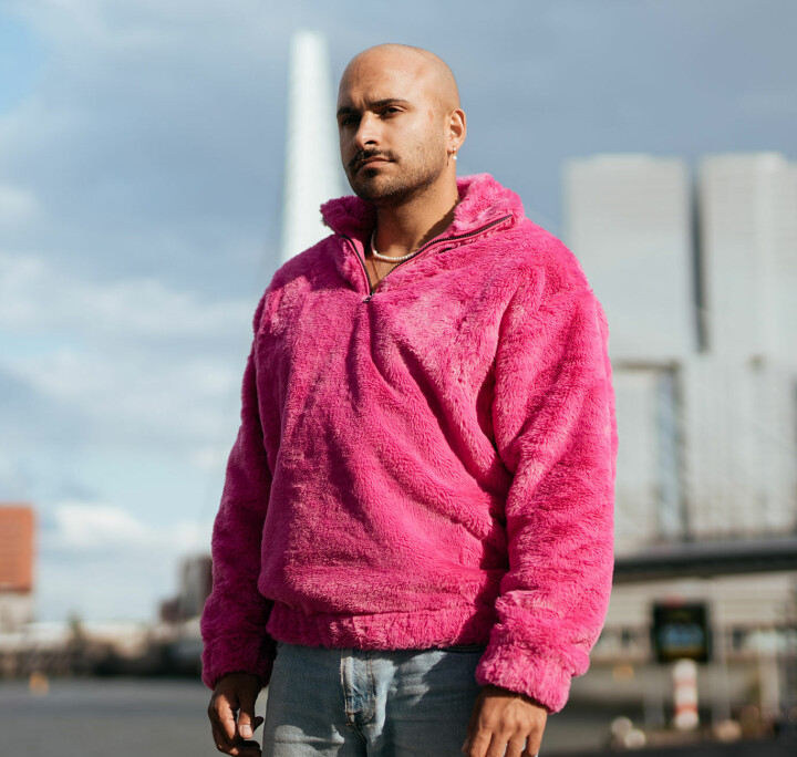 Deze gure, conservatieve wind zal het nooit winnen van onze roze regenjas Rocher Koendjbiharie in roze trui voor de Erasmusbrug