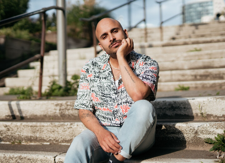 “Zichtbaar queer zijn geeft hoop aan de generaties na ons” Rocher Koendjbiharie in overhemd met korte mouwen op trap in de zon