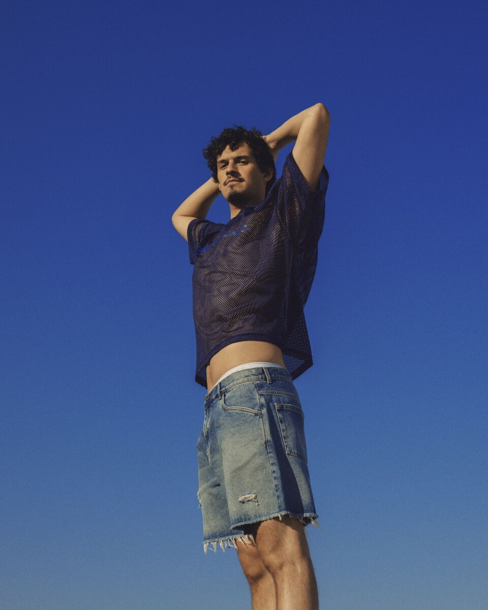 Top: Erl | shorts: Balmain Omar Apollo met armen achter zijn hoofd