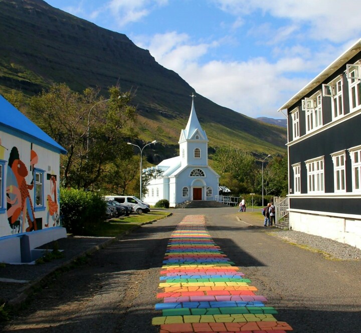 IJsland is het veiligste land ter wereld voor lhbtiq+-personen: van 9 naar 1 in een jaar tijd Blauwe kerk met regenboogweg in Seyðisfjörður, IJsland