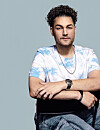 Lorenzo Moinat met gekruiste armen zit op een stoel voor een lichtblauwe achtergrond.