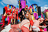 Artiesten in rode en roze kostuums staan op een kleurrijk buitenpodium tijdens Milkshake festival.