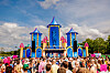 Menigte staat voor een kleurrijke festivalopstelling tijdens Milkshake Festival 2025 met hoge blauwe en roze torens.