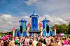 Menigte staat voor een kleurrijke festivalopstelling tijdens Milkshake Festival 2025 met hoge blauwe en roze torens.