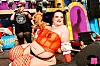 Performers in opvallende kleding op een kleurrijk podium tijdens Milkshake Festival met grote decorstukken en felgekleurde achtergronddetails.