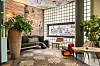 Moderne lobby met banken, grote planten, houten tafels en een rasterraam.