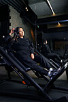 Dinah Bons in zwarte sportkleding zit achterover op een schuine trainingsstoel in een moderne sportschool.