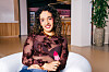Yasmin zit lachend in een witte stoel in een moderne lobby.