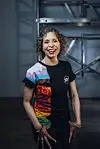 Pride-vrijwilliger Ruchama in een zwart shirt met kleurrijk dessin staat in een industriële ruimte met metalen buizen.