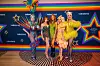 Vier queens en Yildiz Siskens in uitbundige dragoutfits poseren voor een kleurrijke muur met sterren en Videoland-logo’s.