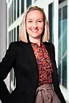 Heather Campbell in zwarte blazer en kleurrijke blouse bij moderne kantoorramen.