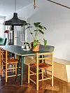 Eetruimte met houten tafel, rotanstoelen, hanglampen en kamerplanten bij een lichte muur.