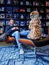 Man in fauteuil kijkt naar een ruwharige hond in een kamer met boekenkasten.