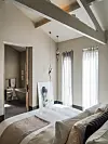 Lichte slaapkamer met groot bed, hoge ramen en open doorgang naar een badkamer.