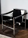 Zwart-witte fauteuil met metalen frame op een donkere houten vloer.